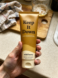 A hand holding the Keep It Down tube in a kitchen, showing its size